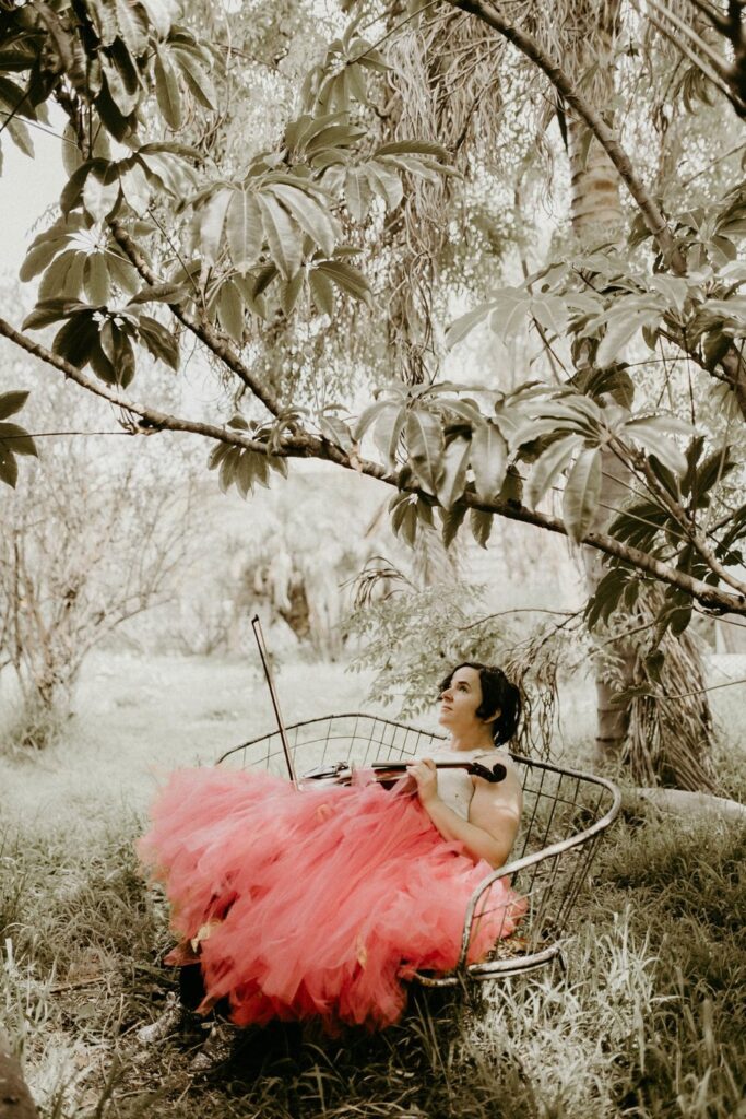 Anna Zinova holding a guitar on a porch in a red tulle skirt